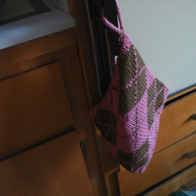 Brown and pink argyle potholder hanging on an oven