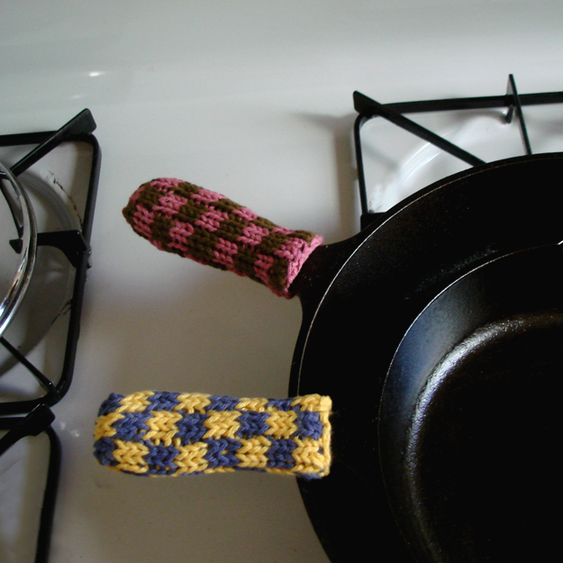 Knitted cozies - pink and brown, and blue and yellow, on cast iron handles on a stovetop
